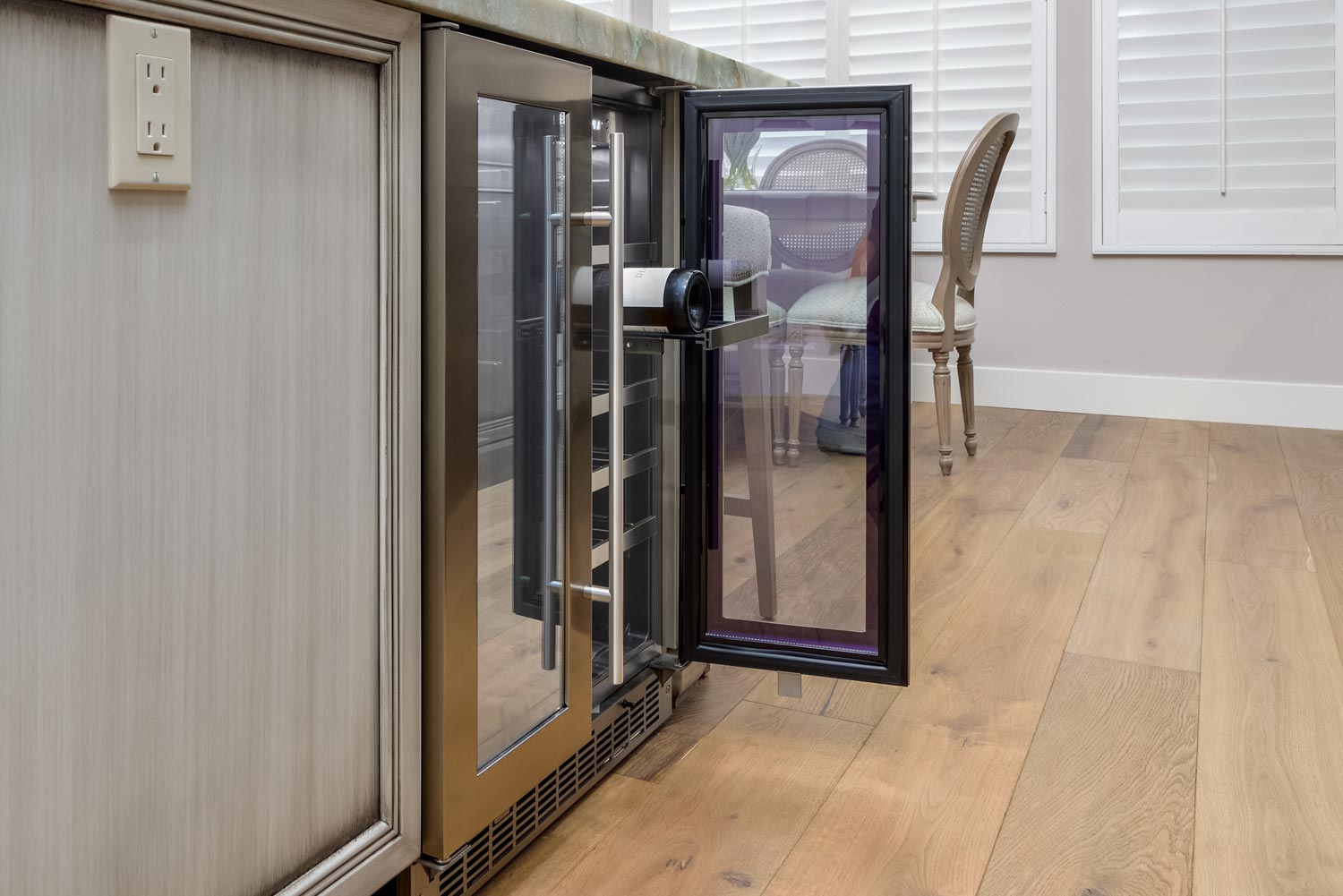 Built-in glass wine cooler beside a kitchen island in a bright hardwood-floored room