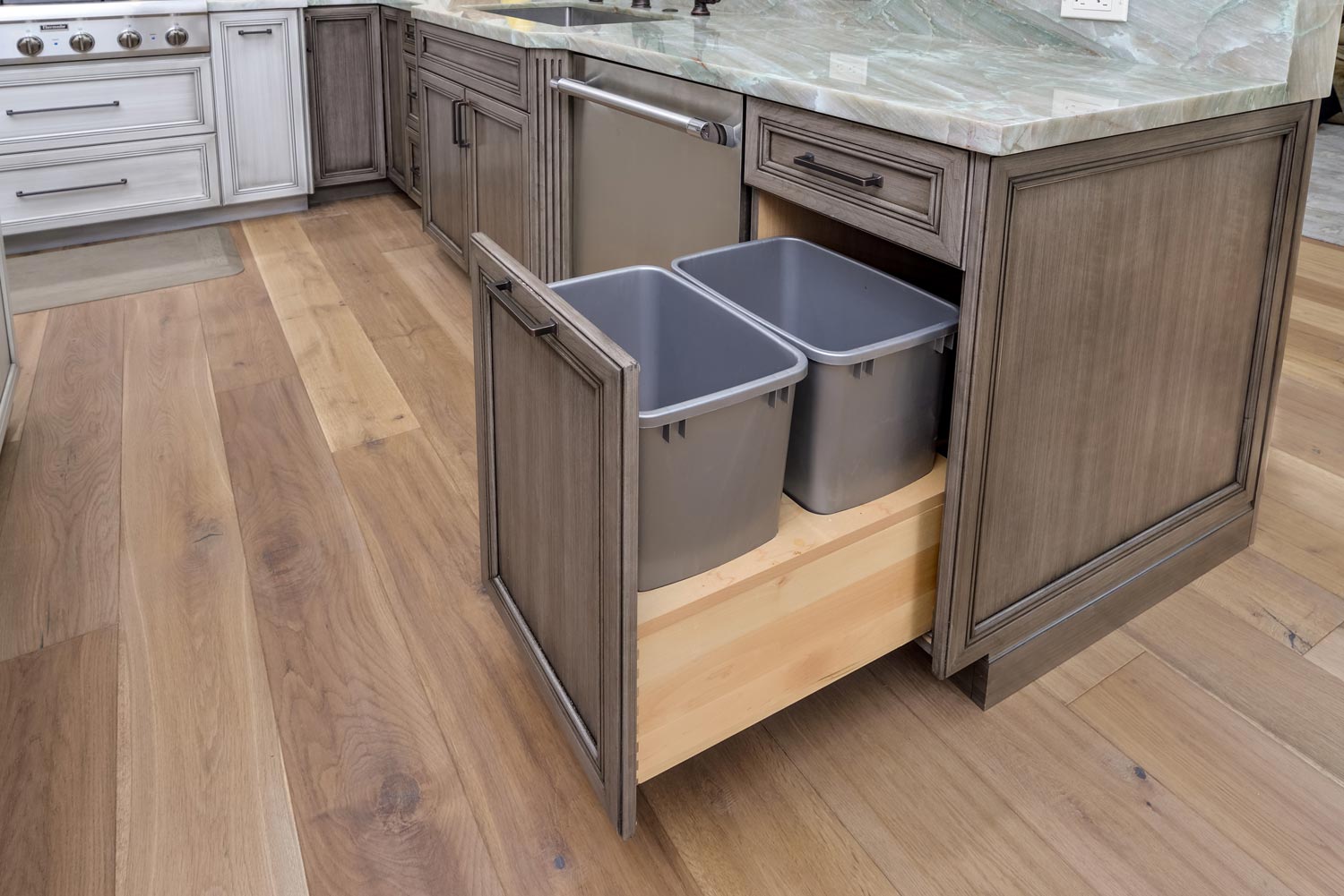 Open kitchen island drawer with two gray trash bins inside