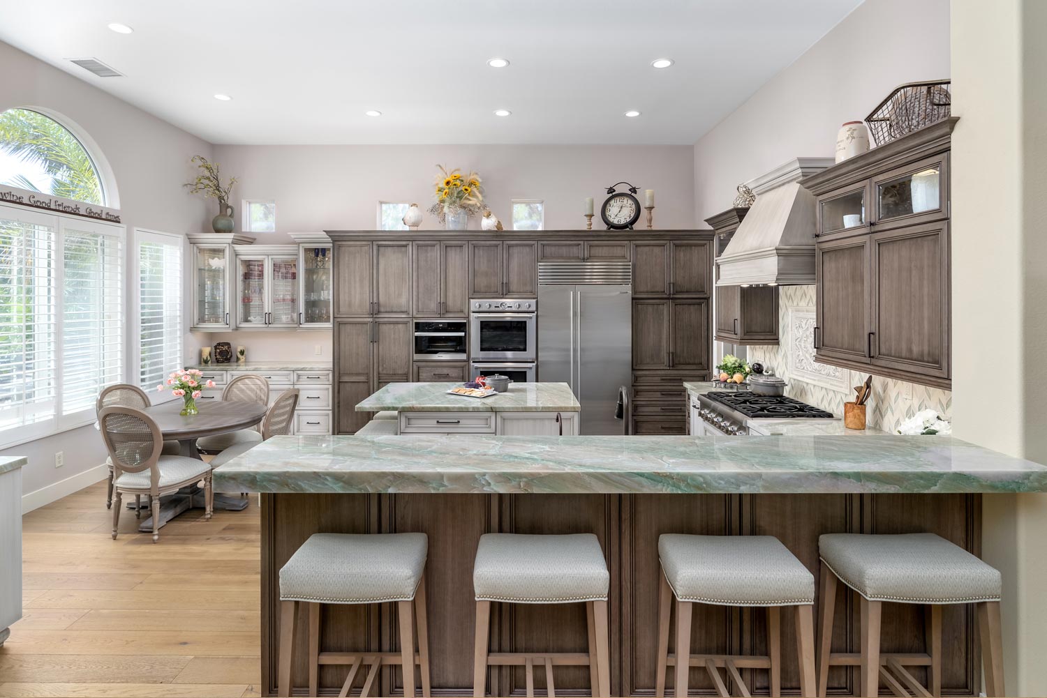 Bright kitchen with large island, four stools, wooden cabinets, and built-in oven near a breakfast nook