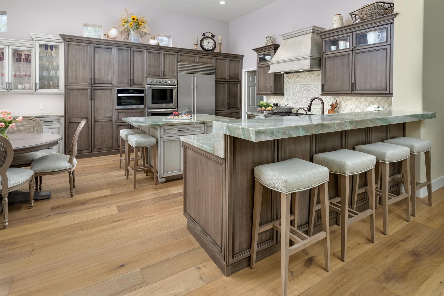 Spacious modern kitchen with gray cabinets, a large island, and four stools on light wood floors