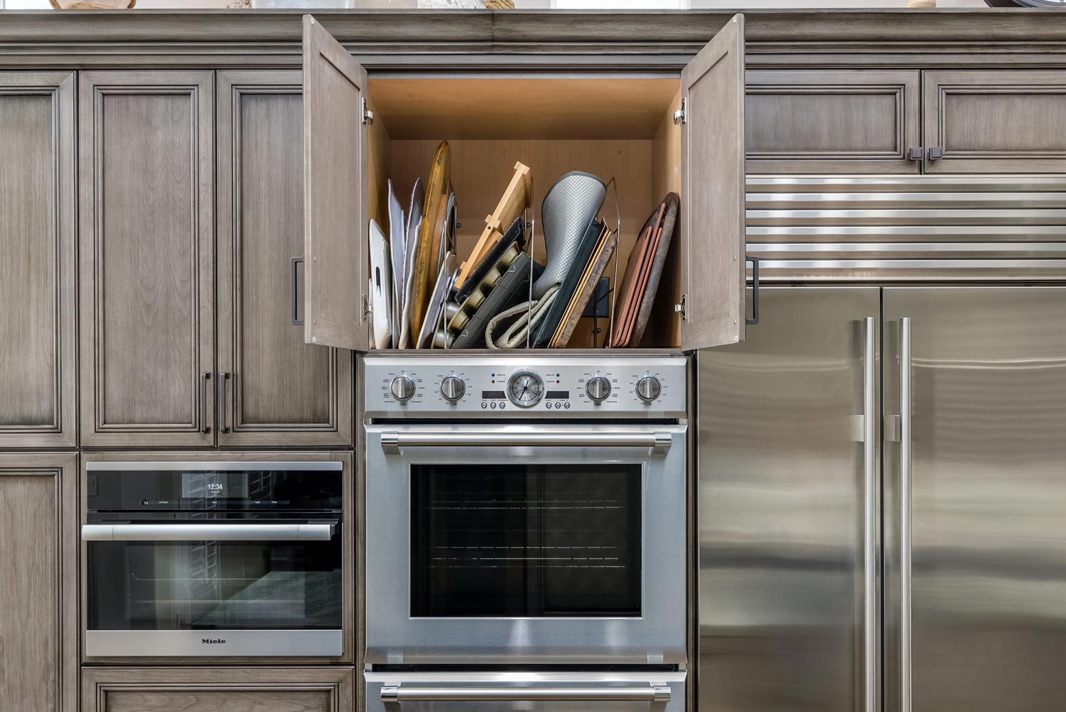 Kitchen cabinets open above a built-in oven, revealing many baguettes stored inside.