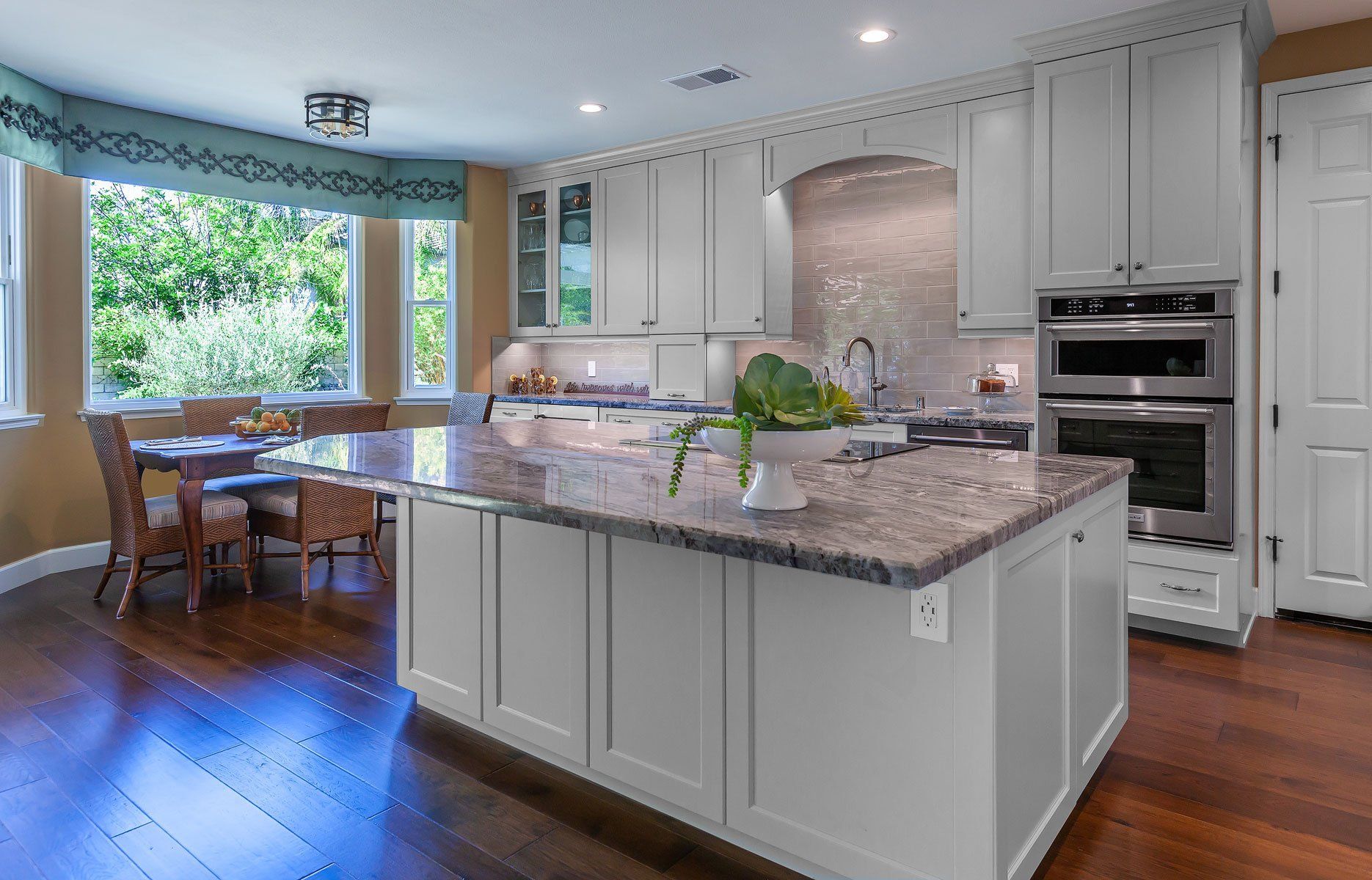 Bright modern kitchen with white cabinets, gray island, granite counters, and a window dining nook