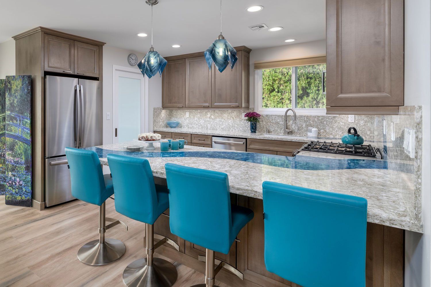 Modern kitchen with granite island, teal barstools, stainless fridge, and blue pendant lights