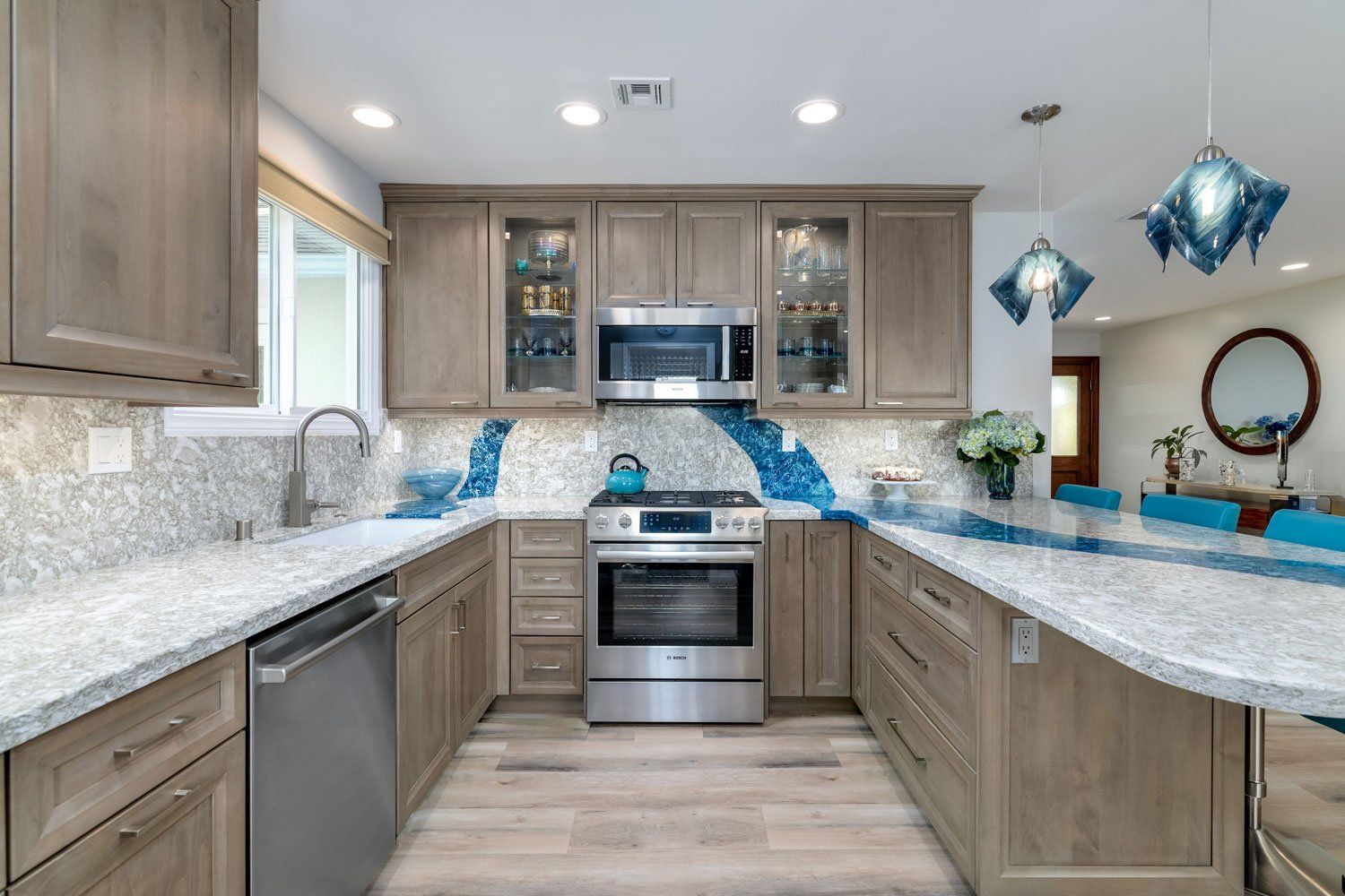 Bright modern kitchen with gray cabinets, white countertops, stainless steel appliances, and blue pendant lights