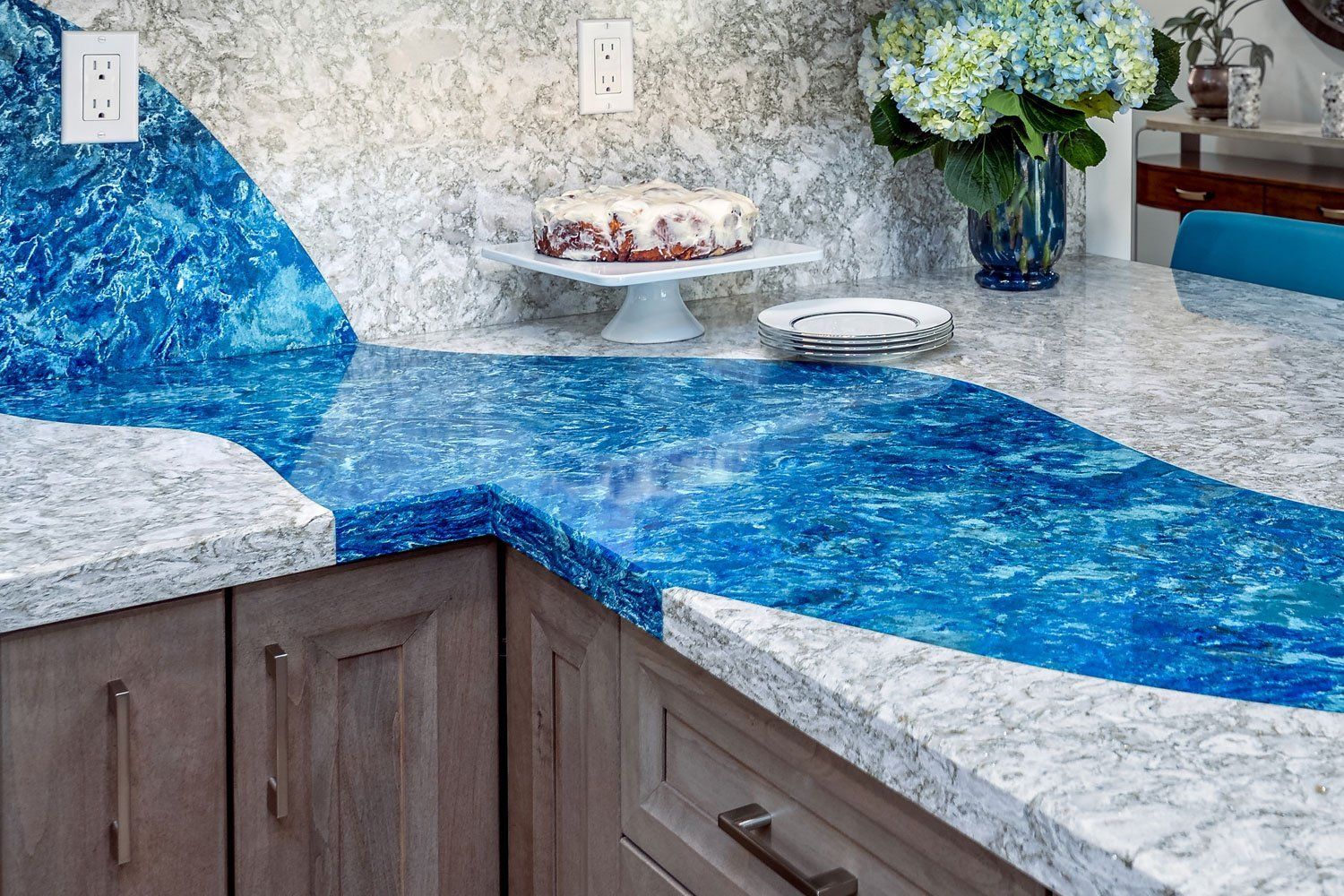 Blue and gray speckled kitchen countertop with a bright blue epoxy river design and flowers in the background