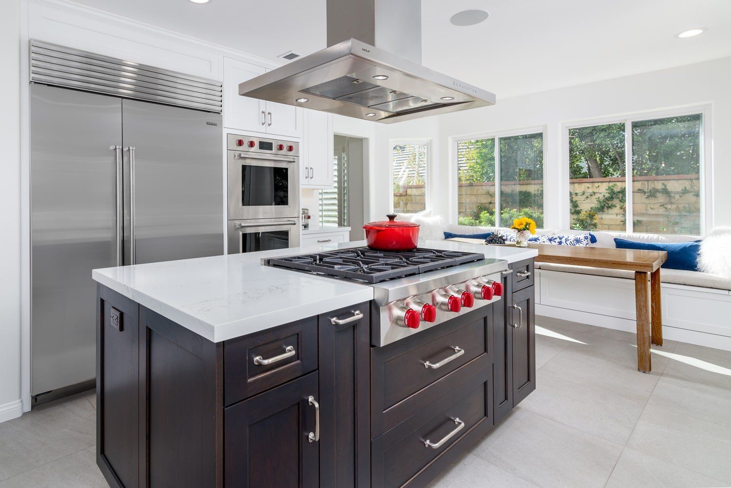 Modern kitchen with stainless steel appliances, dark island, white countertops, and a window-side table.