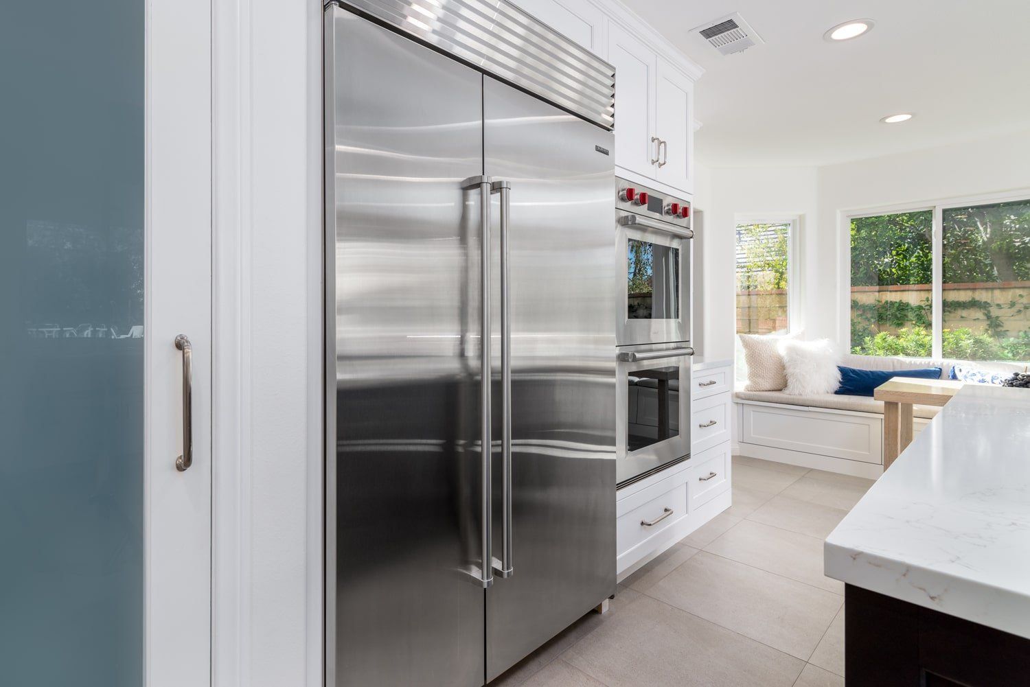 Bright modern kitchen with stainless steel refrigerator, white cabinets, and a sunlit window seat