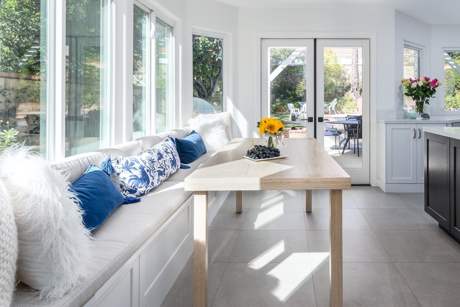 Bright sunroom with white sofa, blue pillows, and a table by large windows and glass doors