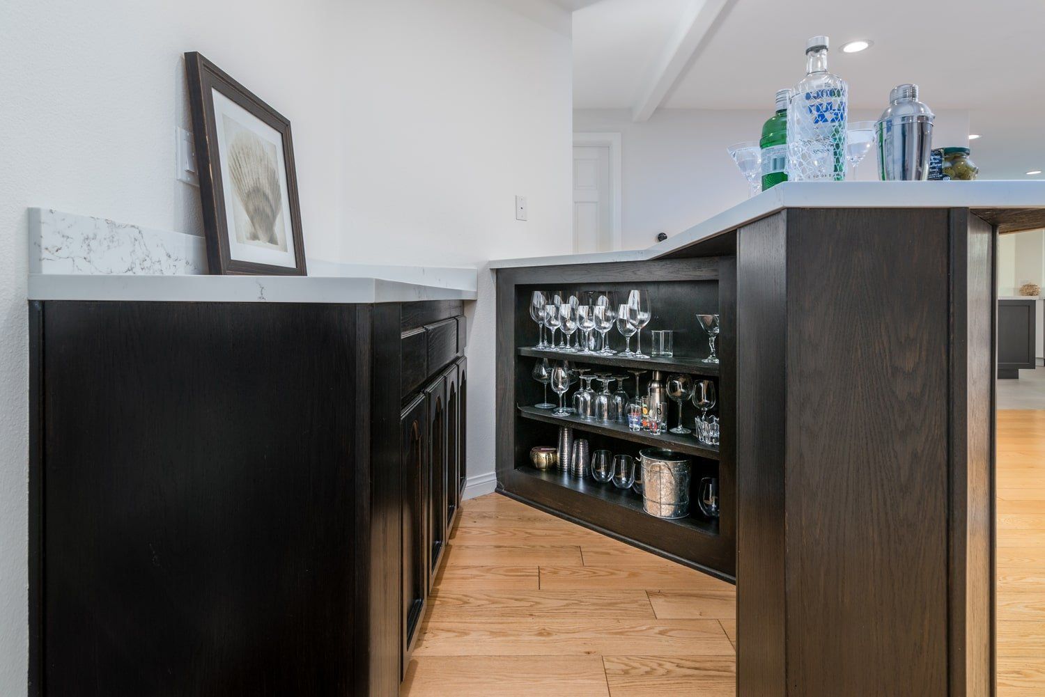 Modern bar area with dark cabinets, glassware, and bottles on a wood floor