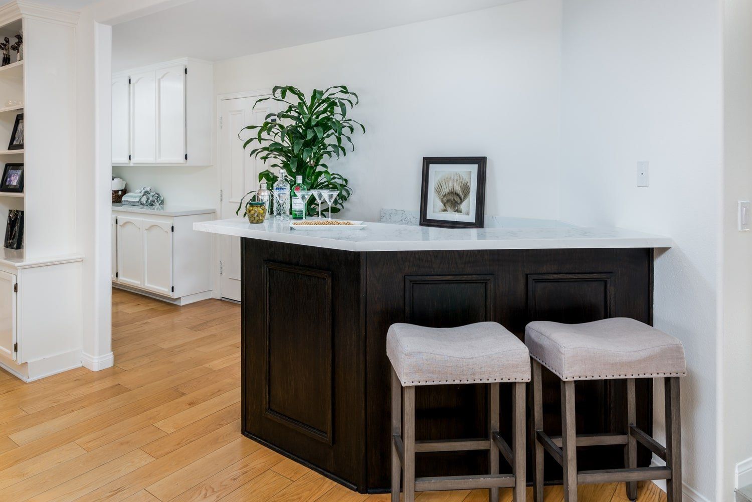 Bright kitchen with dark island, two stools, white cabinets, and hardwood floors