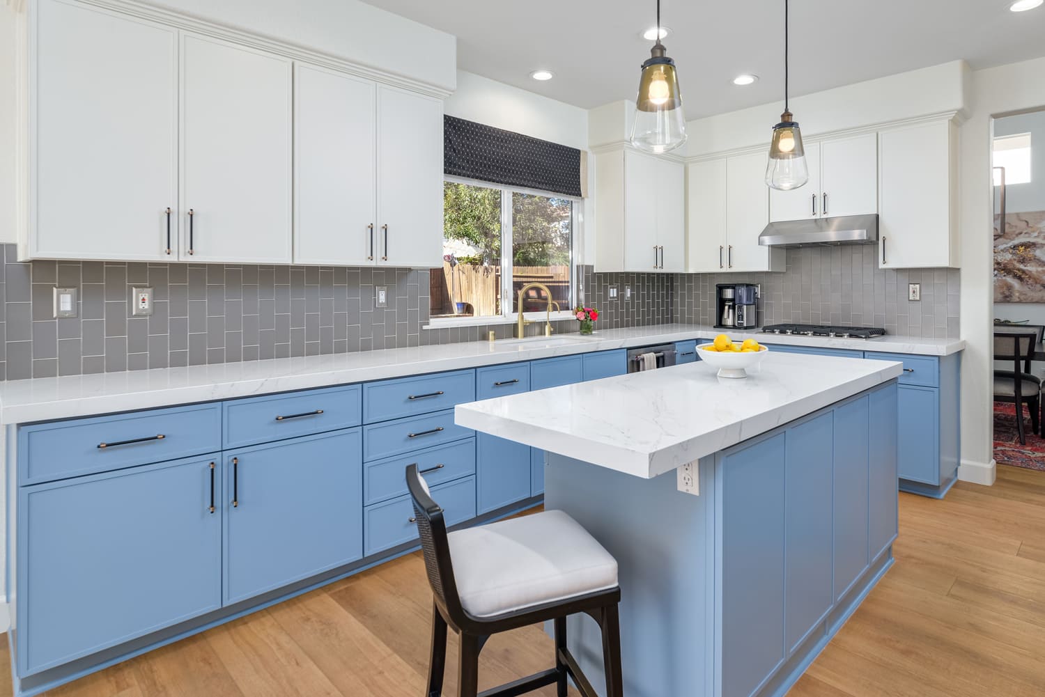 Bright modern kitchen with blue lower cabinets, white countertops, island, and pendant lights