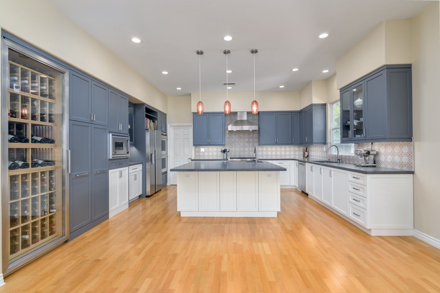Modern kitchen with blue-gray cabinets, white island, stainless appliances, and hardwood floors