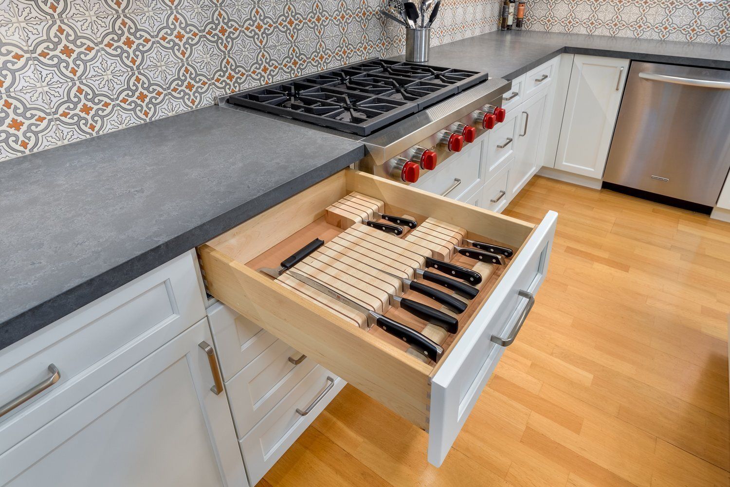 Kitchen drawer with neatly arranged knives and utensils under a stovetop and gray countertop.