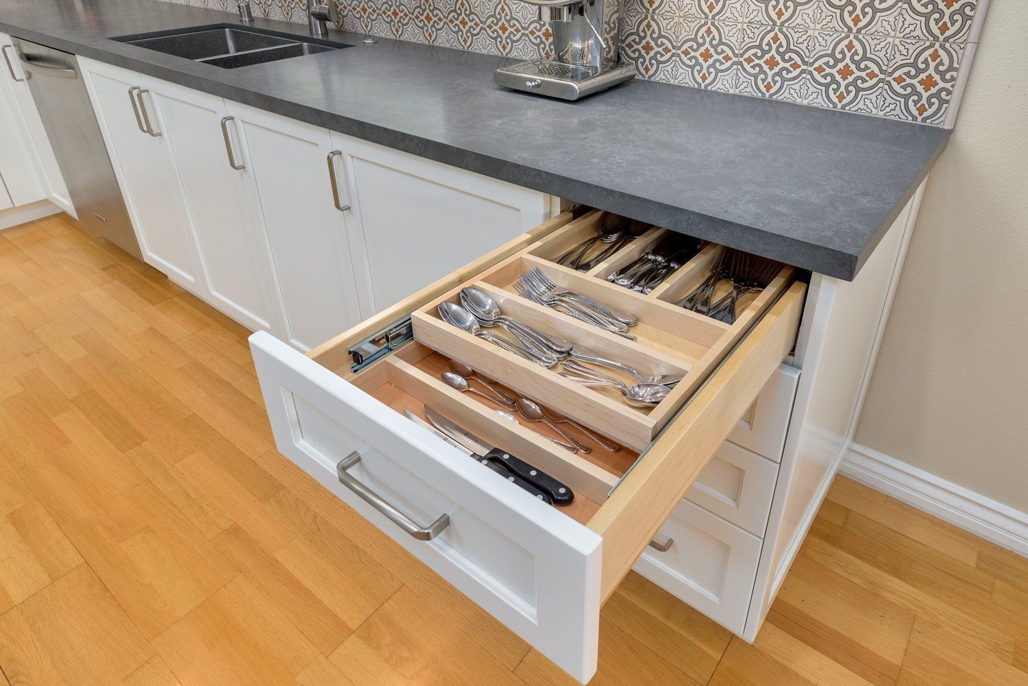 Open kitchen drawer with organized cutlery inserts under a dark countertop
