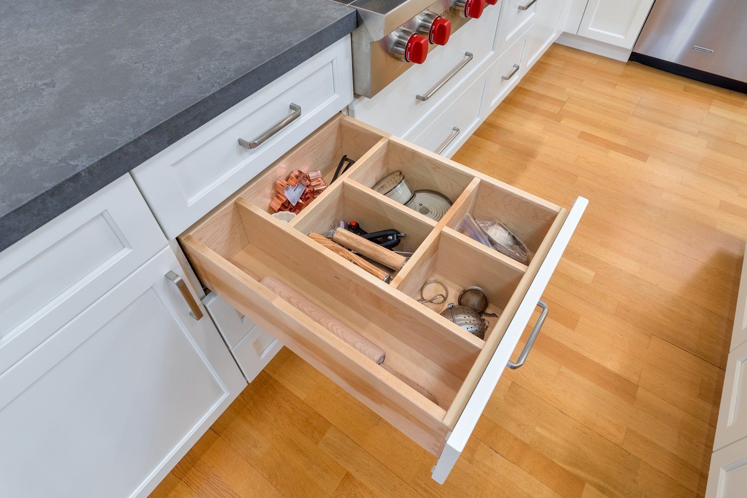 Open kitchen drawer with organized wooden spice and utensil dividers in a white cabinet.