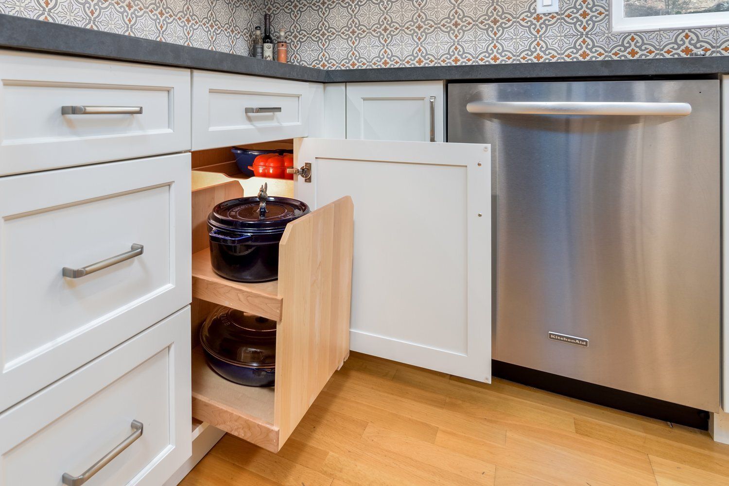 Kitchen cabinet with pull-out shelves holding pots and cookware next to a stainless steel dishwasher