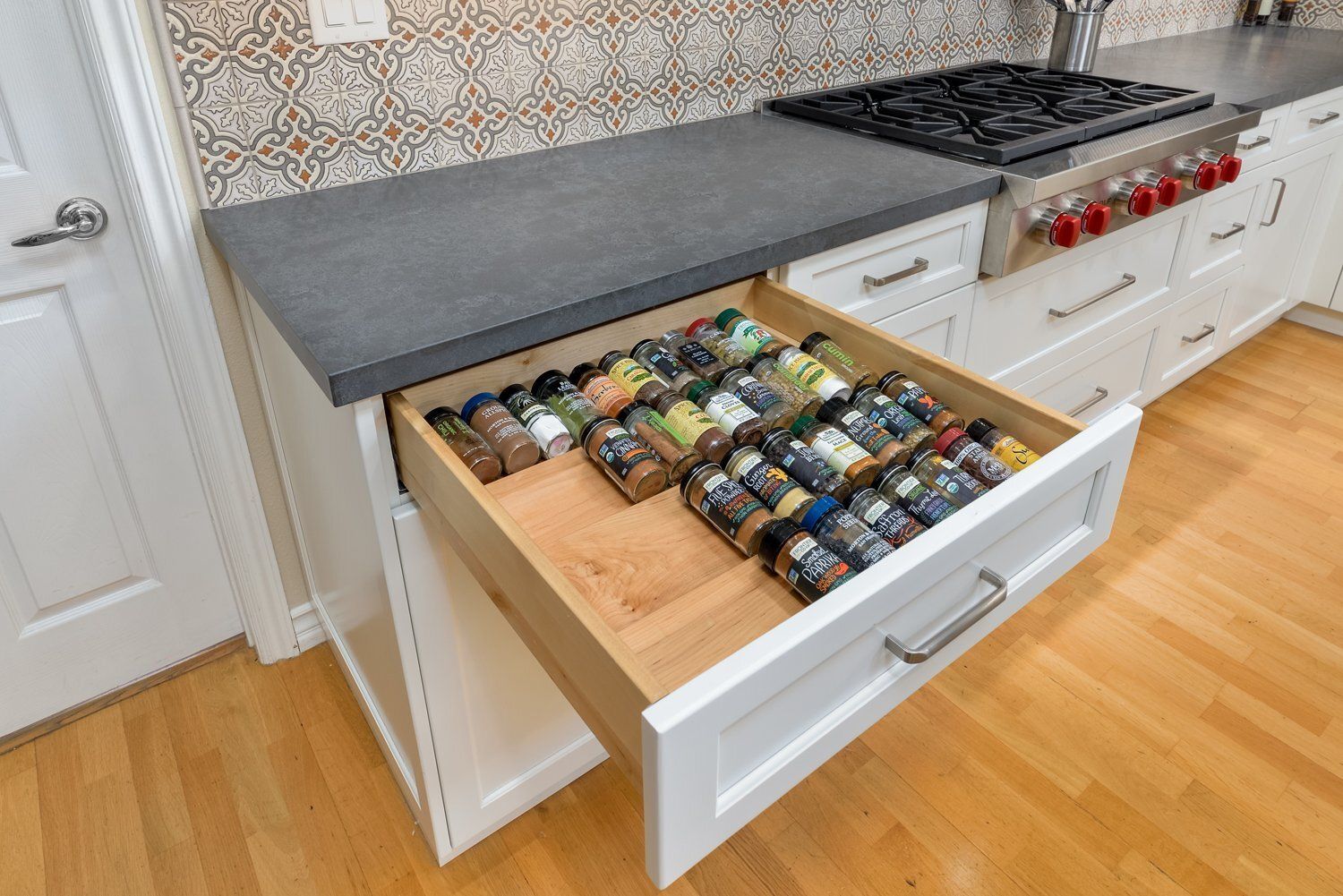 Open kitchen drawer filled with spice jars beside a countertop and stove