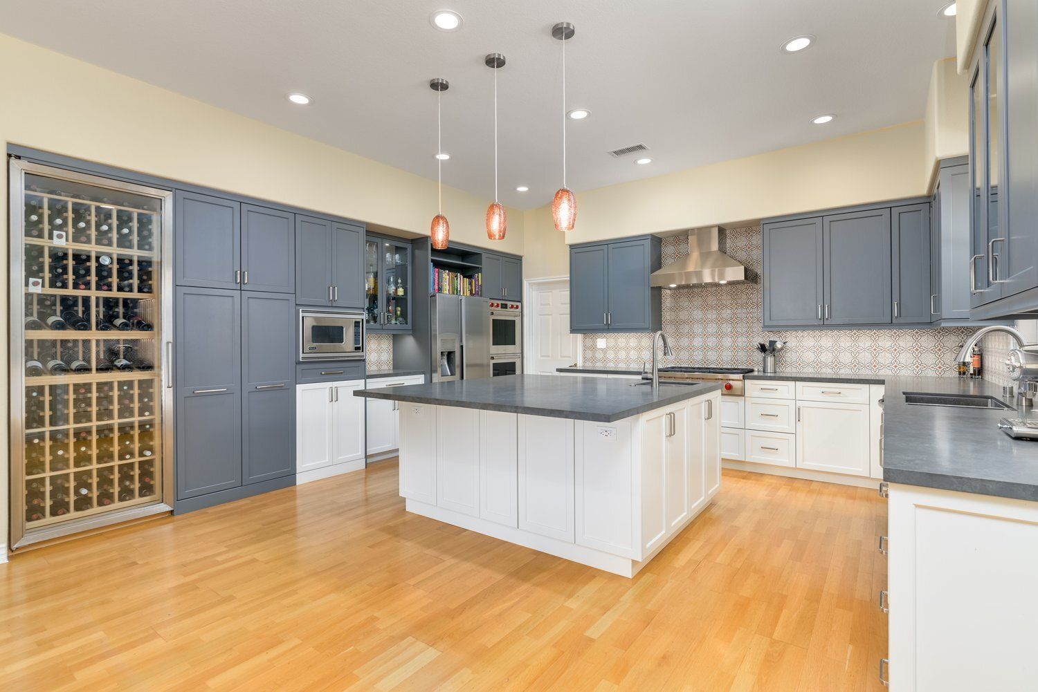 Spacious modern kitchen with blue-gray cabinets, white island, wood floors, and stainless steel appliances