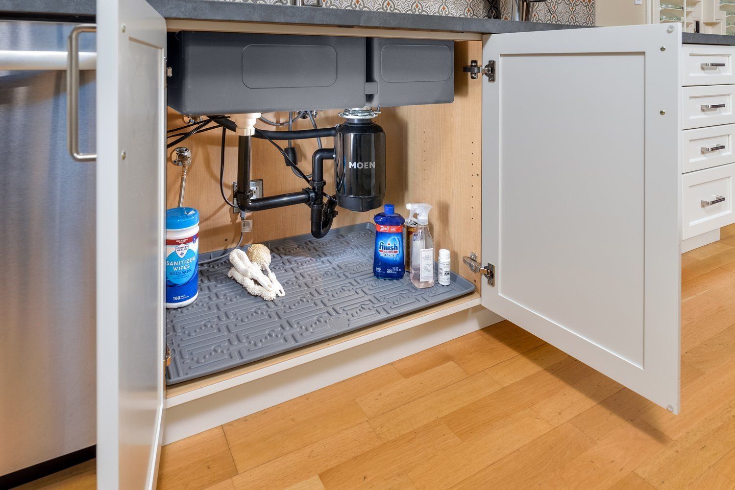 Open cabinet under sink with plumbing, cleaning supplies, and a towel on a gray mat
