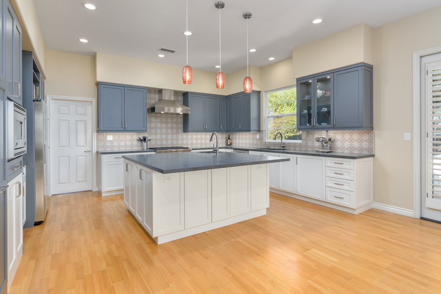 Bright modern kitchen with gray cabinets, white island, tiled backsplash, and hardwood floors