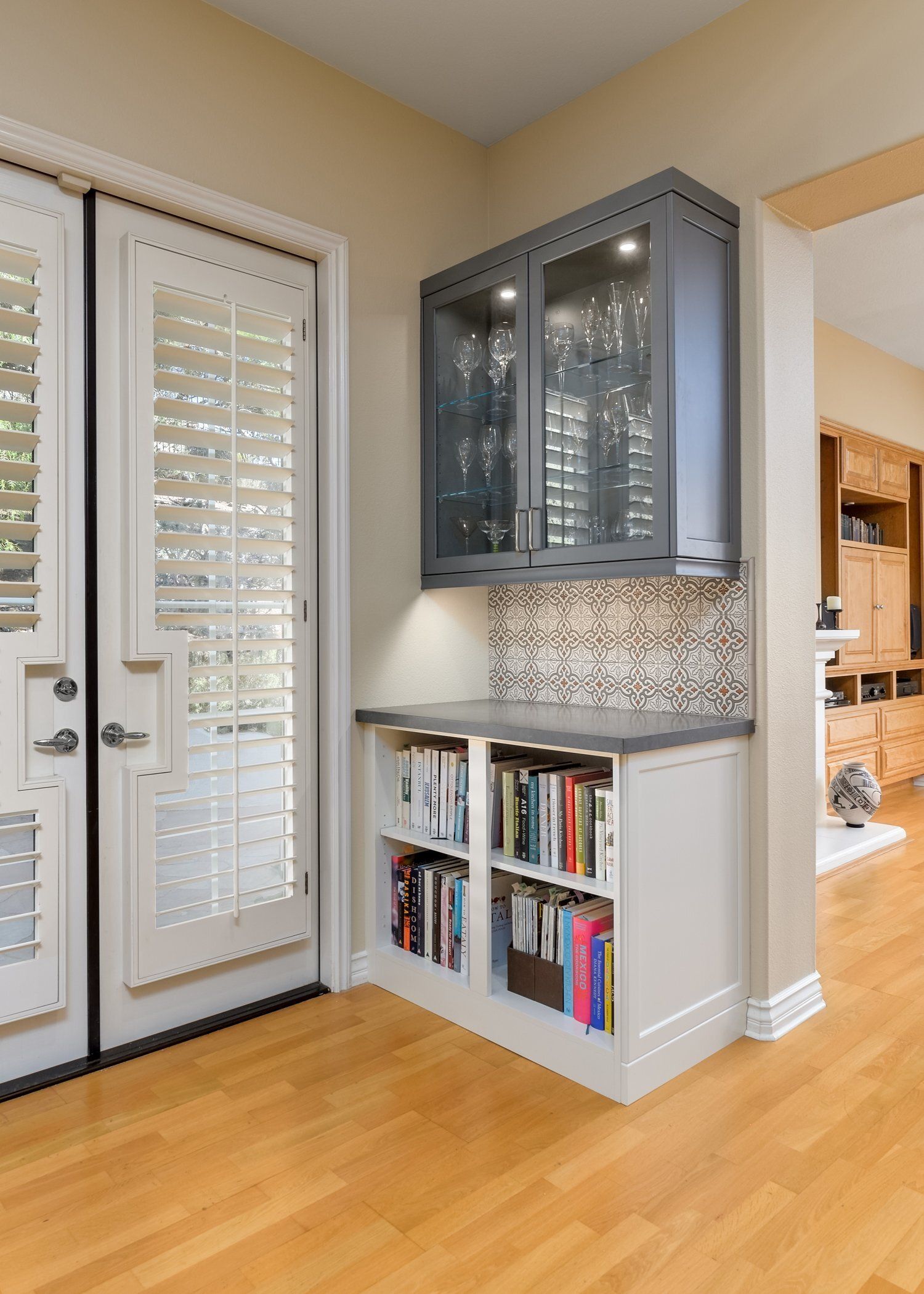 Built-in gray display cabinet over white bookshelves in a bright entryway with French doors and wood floor