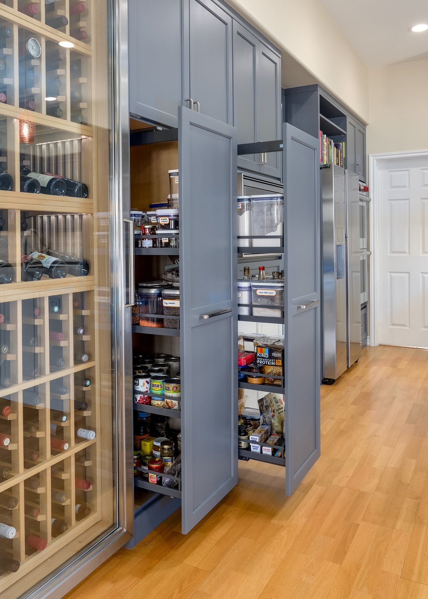 Pull-out pantry cabinets with organized shelves in a bright kitchen corridor
