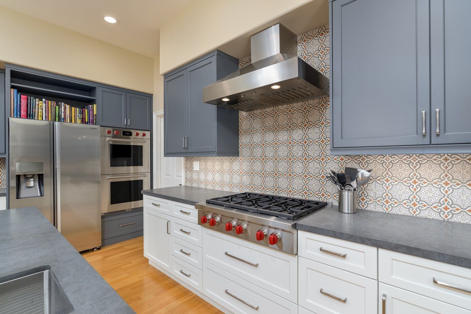 Modern kitchen with stainless appliances, blue cabinets, white drawers, and a patterned backsplash