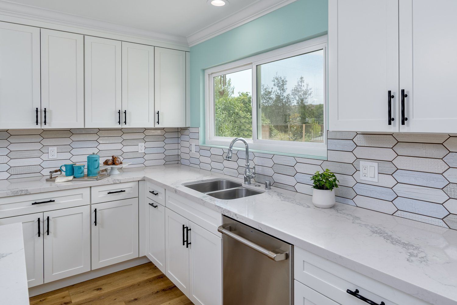 Bright modern kitchen with white cabinets, marble counters, hex tile backsplash, and a window over the sink