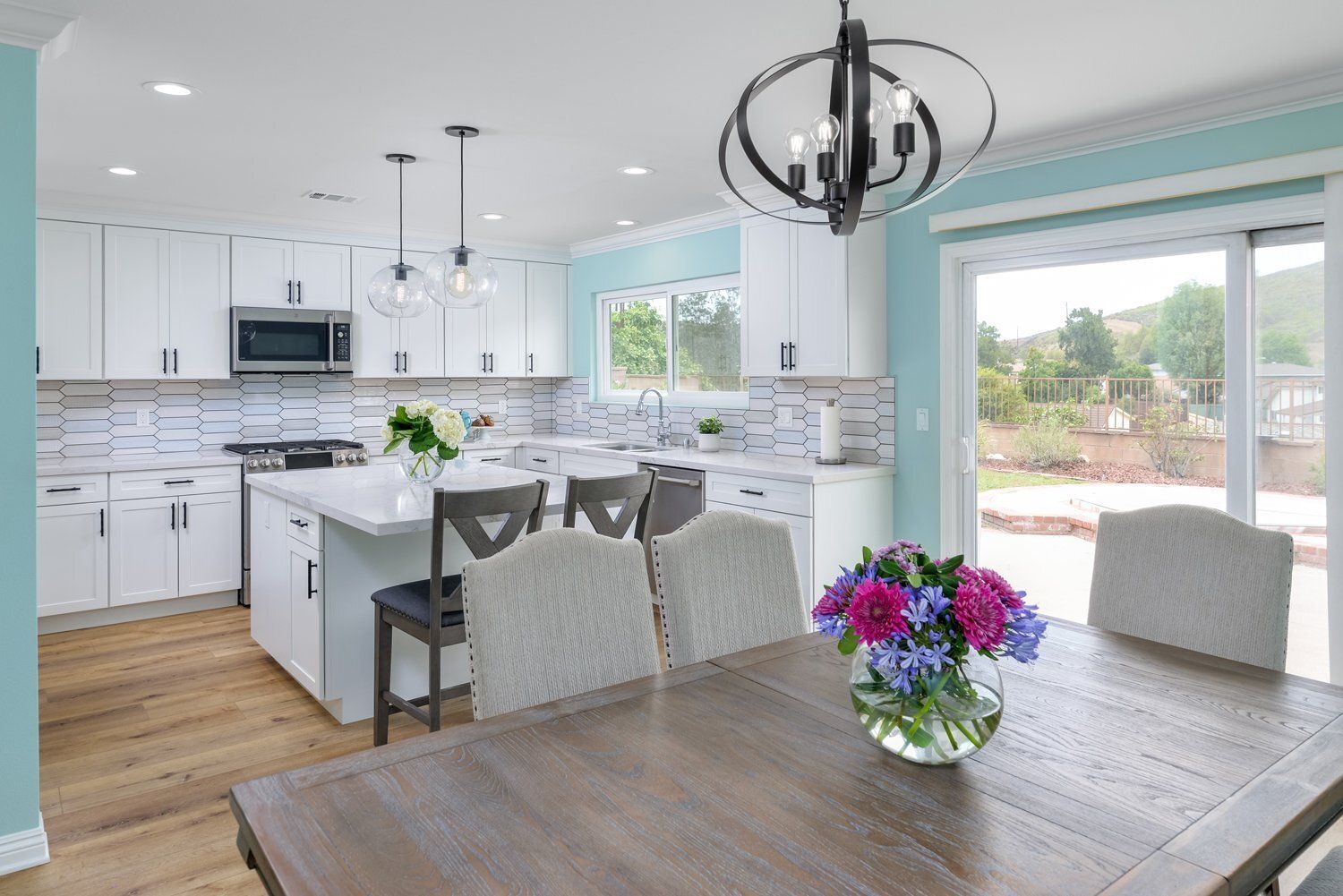 Bright open kitchen and dining area with white cabinets, wood table, and flowers by sliding glass doors