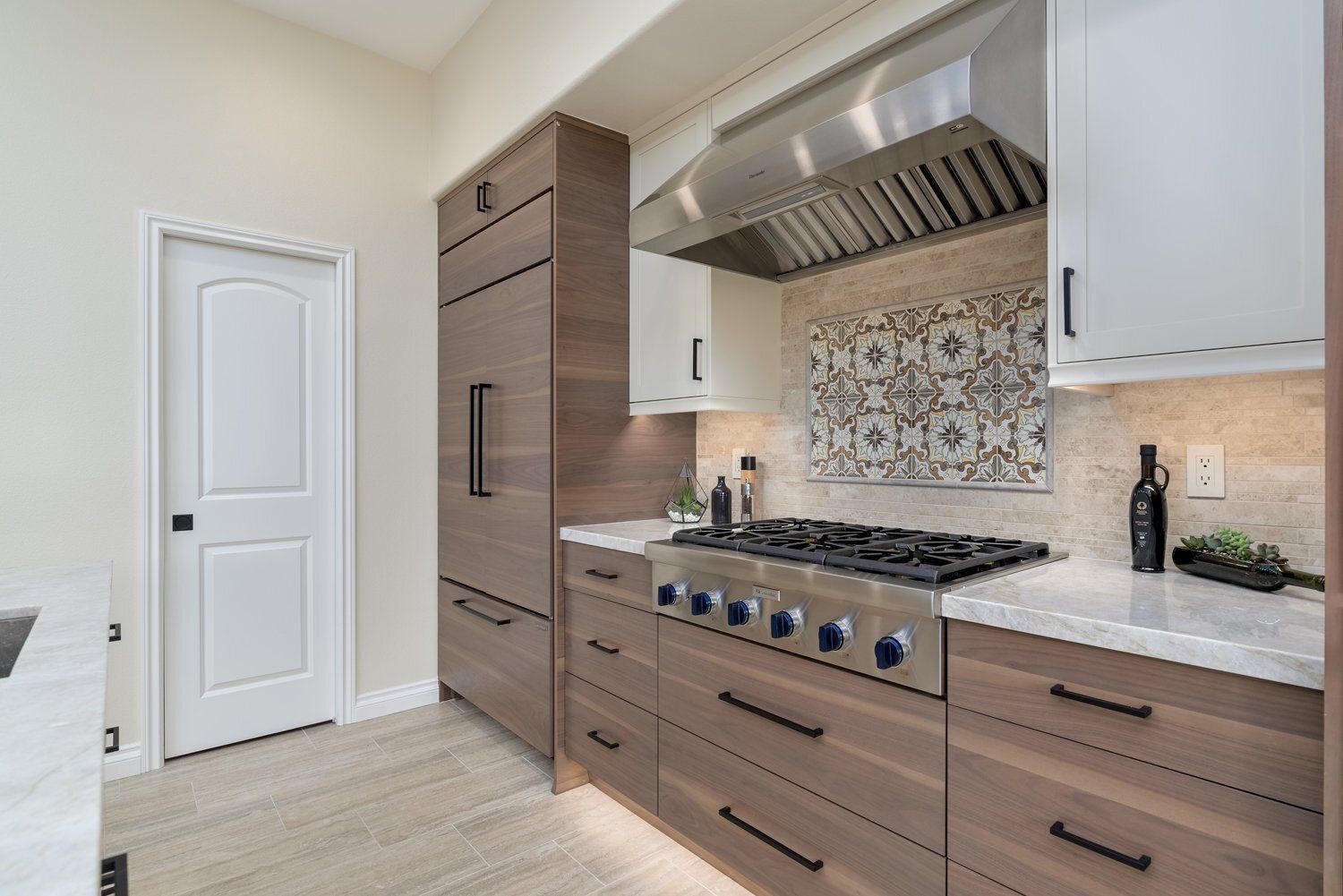 Modern kitchen with white cabinets, wood drawers, stainless range, and patterned tile backsplash.