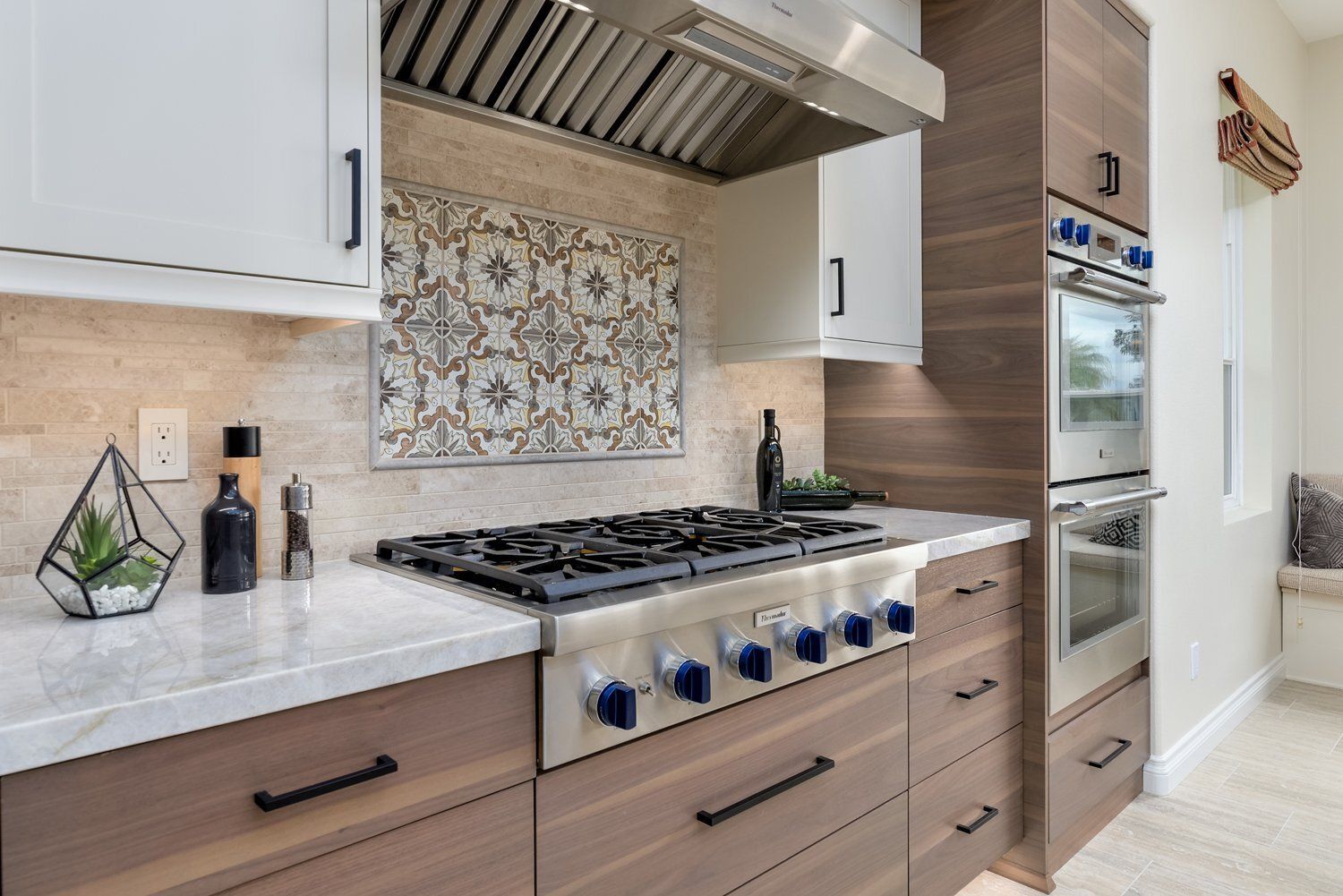 Modern kitchen with white cabinets, stainless range hood, patterned tile backsplash, and blue stove knobs