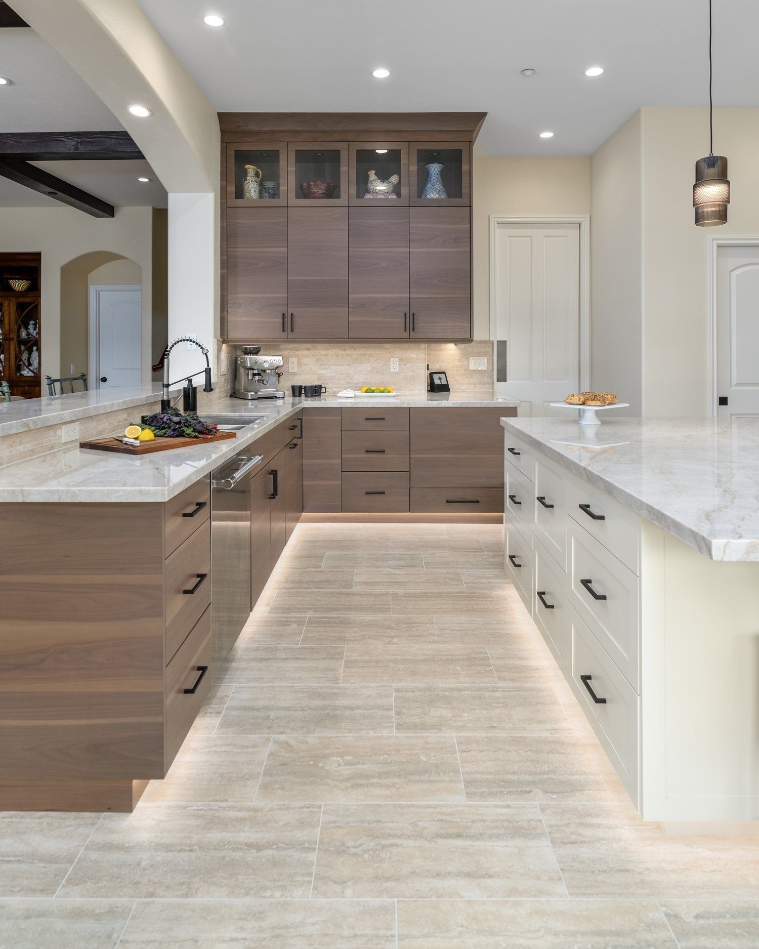 Modern kitchen with light wood cabinets, large island, and white marble countertops, viewed from the center aisle
