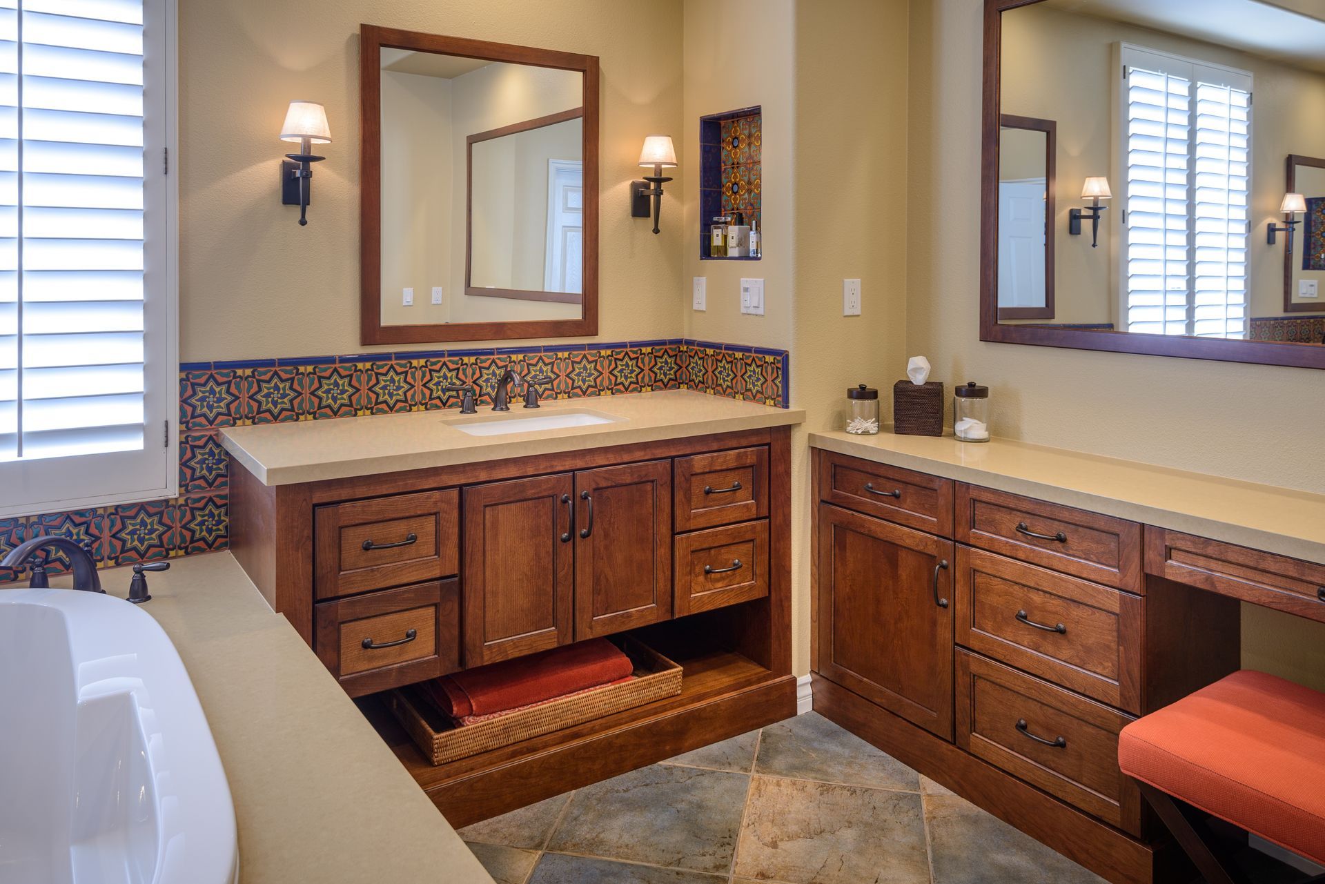 Bathroom vanity with double sinks, mirrors, tiled backsplash, and wooden cabinets in a beige room
