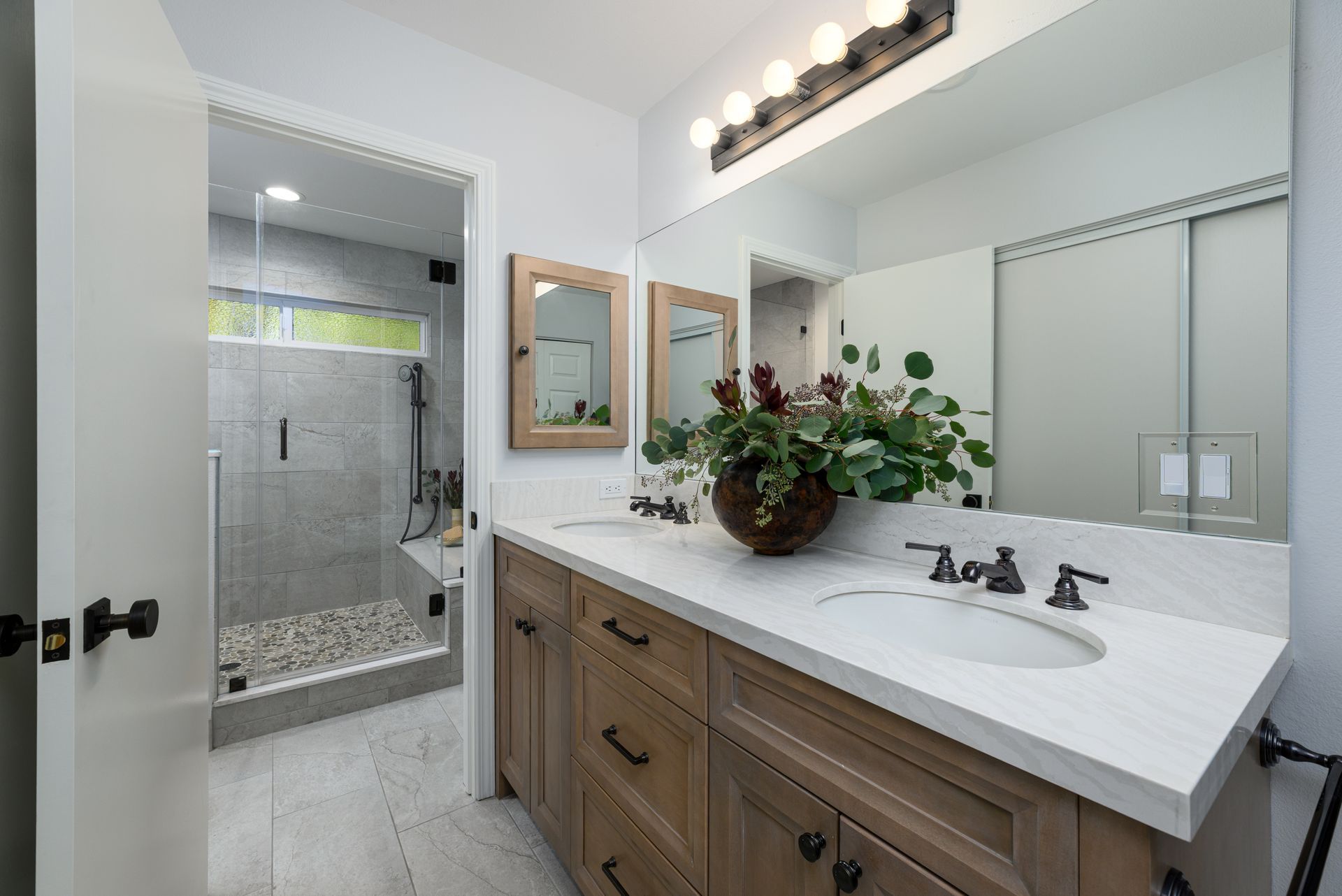 Modern bathroom with wooden vanity, white countertop, large mirror, and glass-enclosed shower