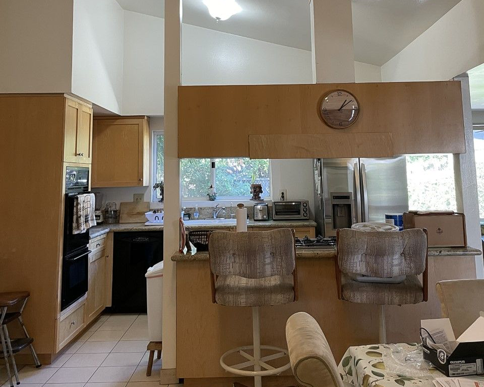 Modern kitchen with breakfast bar, woven stools, and wood cabinets, viewed into a bright open living area