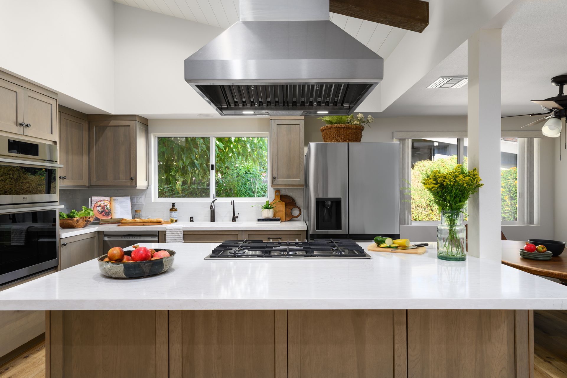 Modern kitchen with white island, stainless range hood, wood cabinets, and flowers by the window