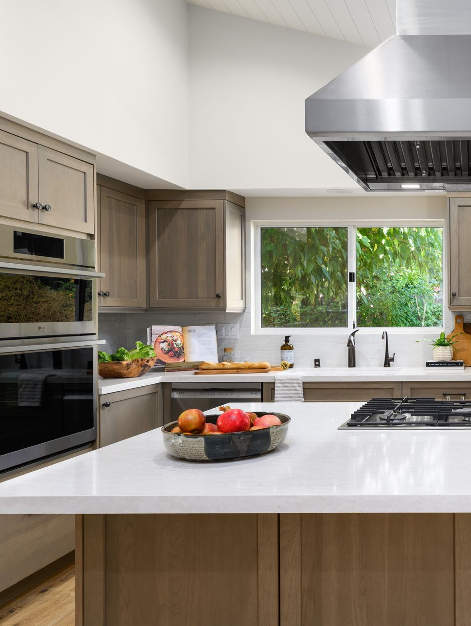 Bright modern kitchen with white island, wood cabinets, stainless hood, and window over sink.