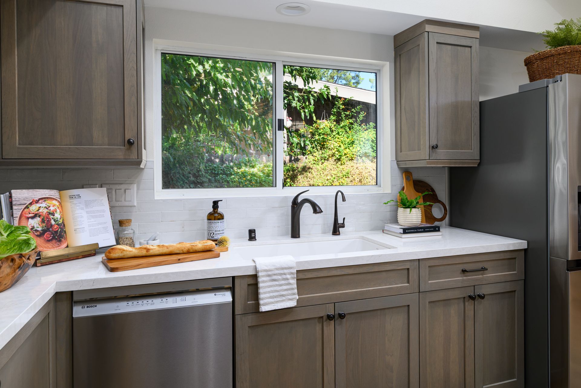 Modern kitchen with gray cabinets, white countertops, sink under a window, and fresh produce on the counter