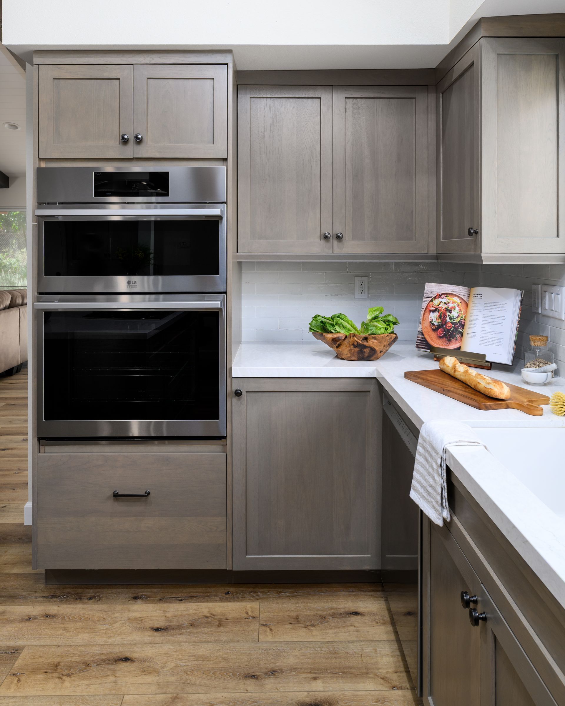 Modern kitchen with light wood cabinets, built-in oven, white countertops, and a fruit bowl on the counter
