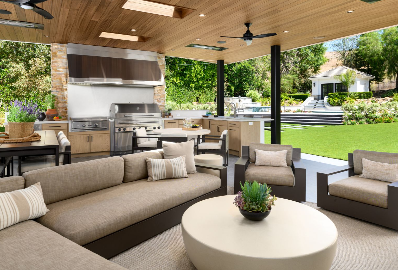 Covered patio with beige seating, outdoor kitchen, and green lawn view