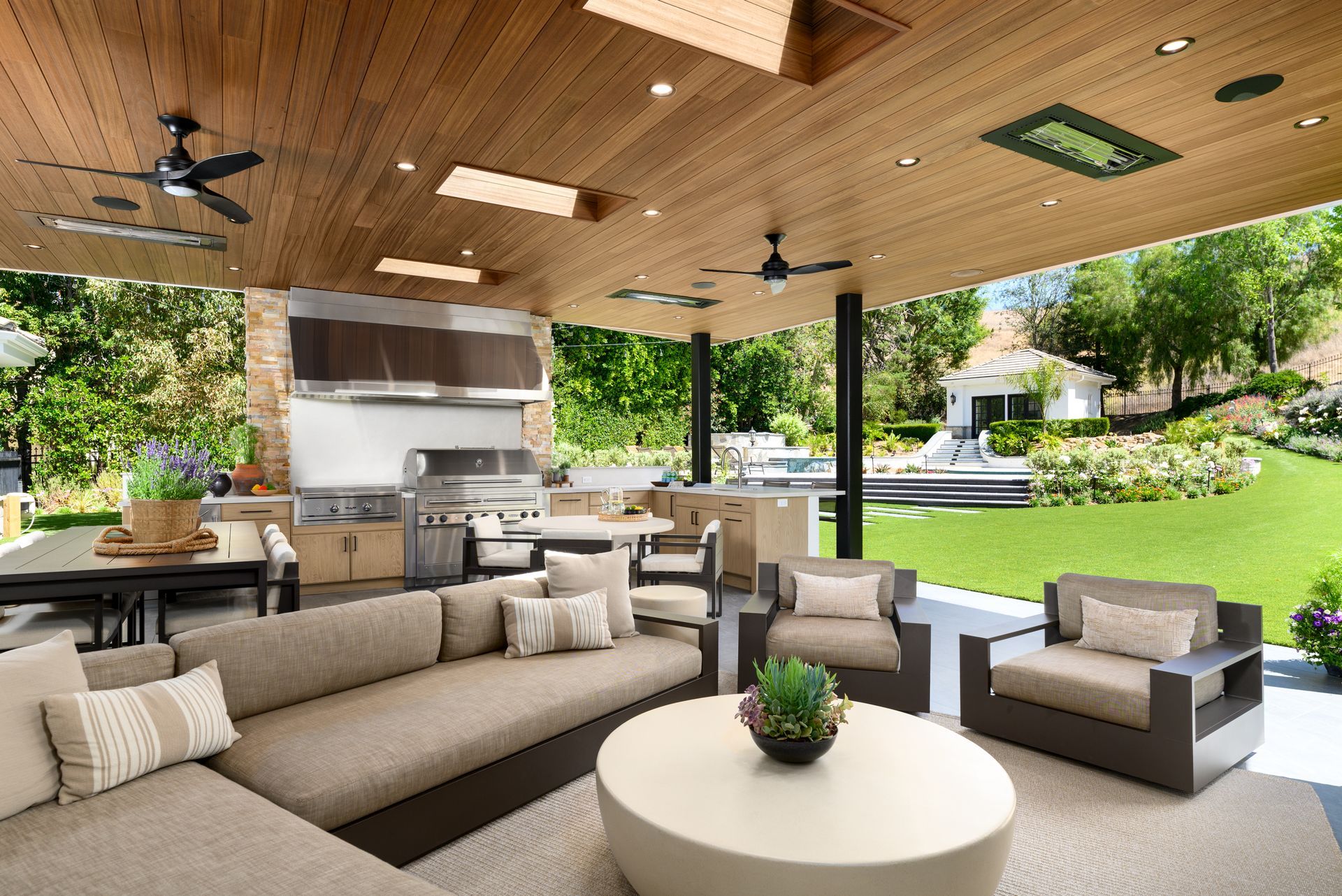 Modern covered patio lounge with beige seating, wood ceiling, and open view of a green backyard.