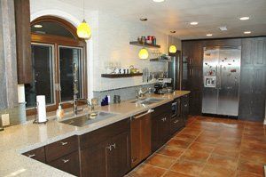 Modern kitchen with dark wood cabinets, granite counters, pendant lights, and stainless steel fridge