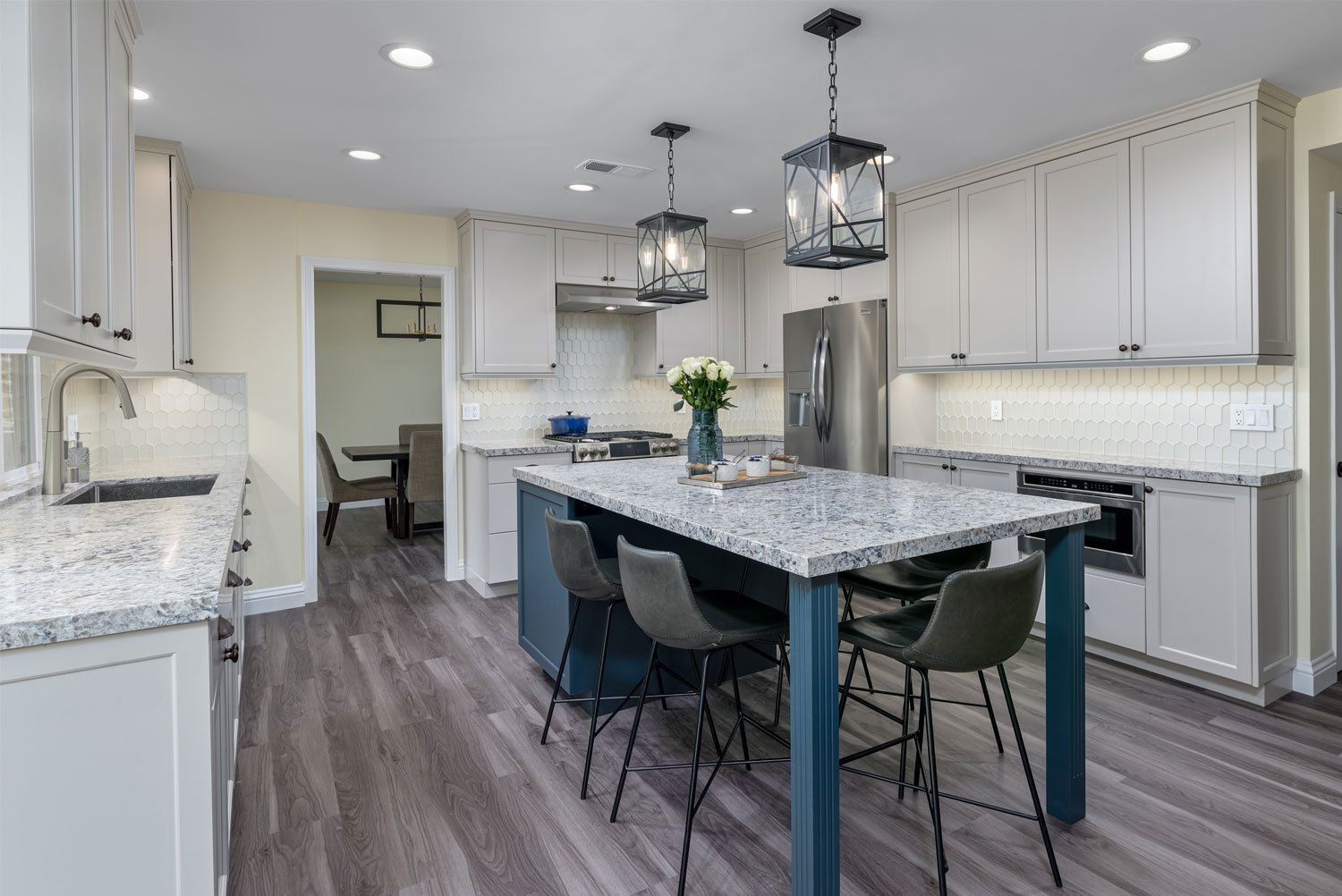 Bright modern kitchen with gray island, pendant lights, white cabinets, and wood-look flooring