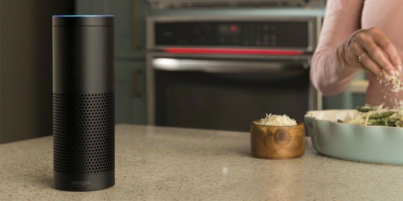 Black smart speaker on kitchen counter beside bowls of food being prepared
