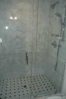 Tiled glass shower enclosure with chrome showerhead and black-and-white mosaic floor.