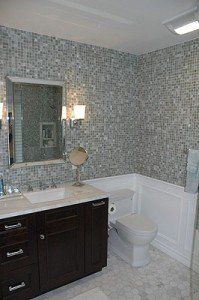 Modern bathroom with dark vanity, mirror, white toilet, and mosaic tile walls with wainscoting