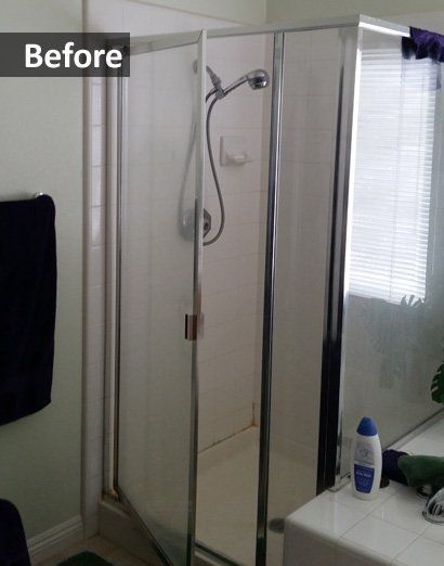 Before view of a bathroom shower with sliding glass doors and a handheld showerhead.