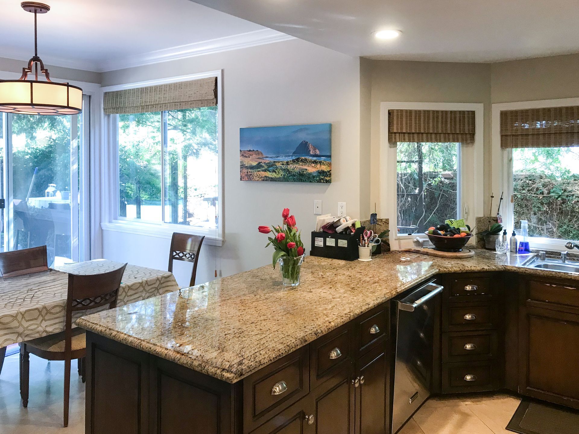 Bright kitchen with granite island, dark cabinets, and dining area by large windows.