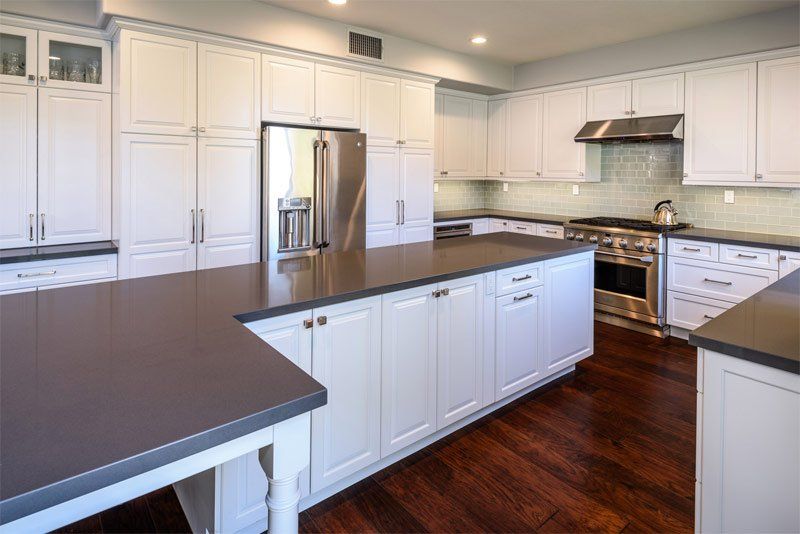 Bright modern kitchen with white cabinets, stainless steel appliances, dark countertops, and hardwood floors