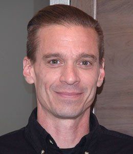 Portrait of a smiling person with slicked-back hair, wearing a black shirt